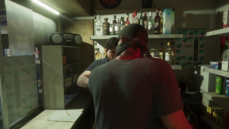 A man in a black cap, grey T-shirt and dark face covering stands with his back to us, facing a shop worker behind a counter in a cramped liquor store.