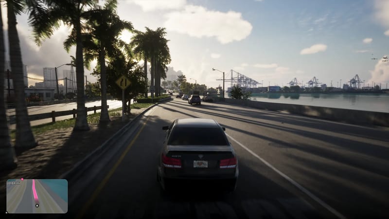 A dark saloon car drives along a palm-lined waterside road towards VC Port's cranes in bright, hazy sunshine.