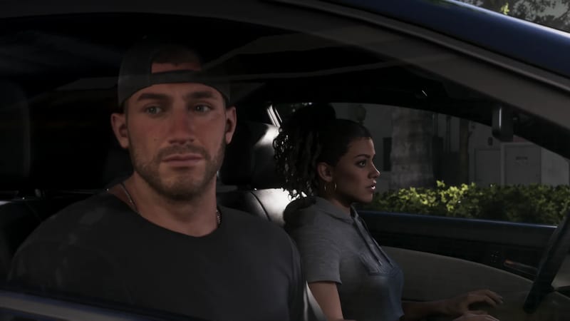 Jason Duval, in a backwards cap and dark t-shirt, sits in a car beside Lucia Caminos, who looks out of the window towards a hedge-lined street.