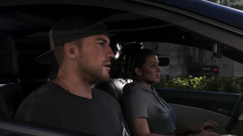 Jason Duval, in a backwards cap and dark T-shirt, and Lucia Caminos, in a grey hoodie, sit in a car on a tree-lined street.