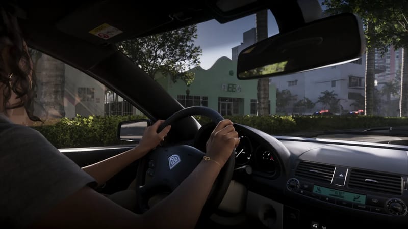 A woman with dark curly hair drives a car with both hands on the wheel, with a green building and palm trees outside on a sunny street.