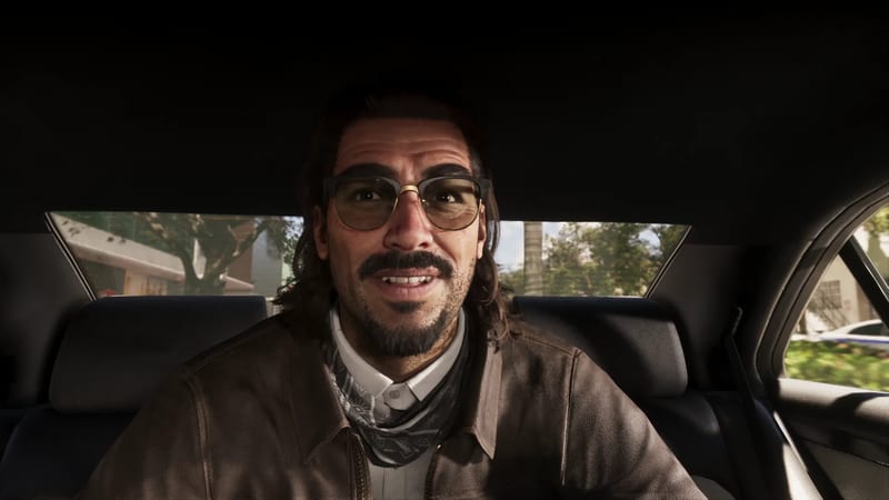 Raul Bautista, a smiling man with glasses and a moustache, sits in the back seat of a car on a sunny, tree-lined street.