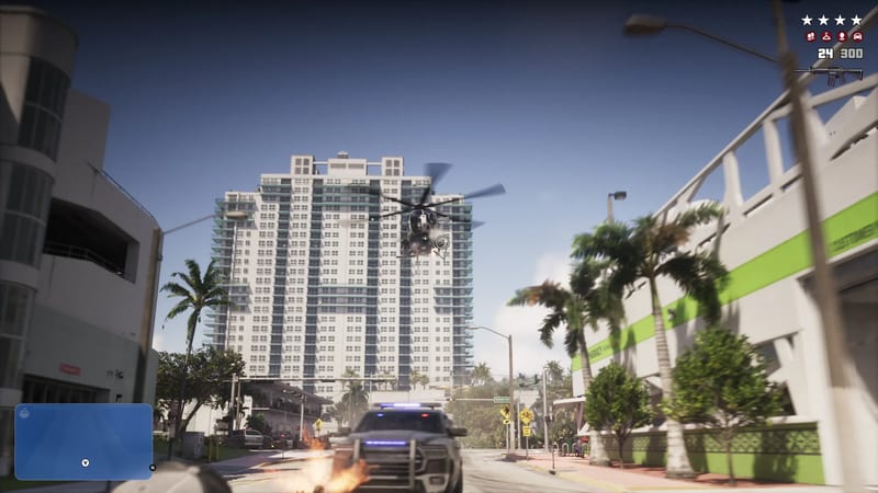 A police helicopter hovers in front of a tall white tower block above a Vice City street, as a police pickup with flashing lights drives towards the viewer.