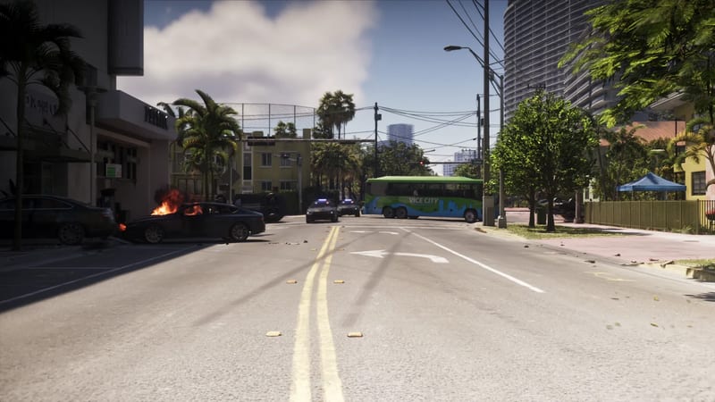 A burning black car and two police cars near a green Vice City bus blocking a sunny street lined with palm trees, with a tall curved tower behind.
