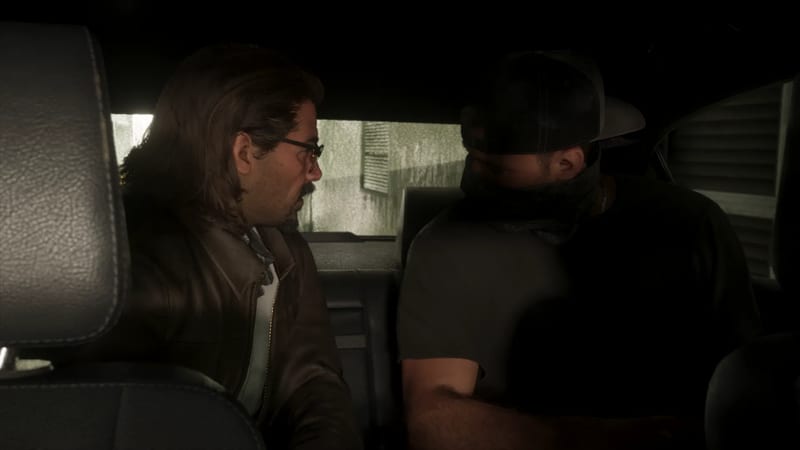 Two men sit in the back of a dark car, one with long hair and glasses turning to look at the other, who wears a cap and a scarf over his face.