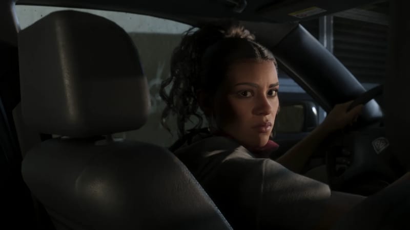 Lucia Caminos looks back over her shoulder from the driver's seat of a car in a dimly lit space, one hand on the steering wheel.