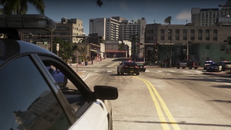 A police car's side mirror and light bar frame a sunny Vice City street, where police cars chase a dark car past palm trees and tall buildings.