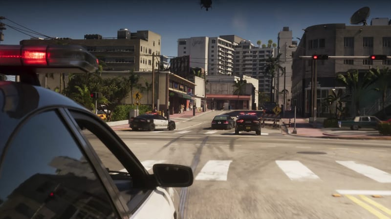 View from a police car with a flashing red light bar, following two police cars and a black saloon along a sunny Vice City street lined with palm trees.