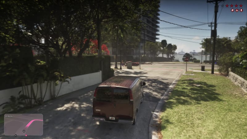 A dark red van drives down a sunny, tree-lined residential street towards a junction with a stop sign and a stretch of water beyond, in Vice City.