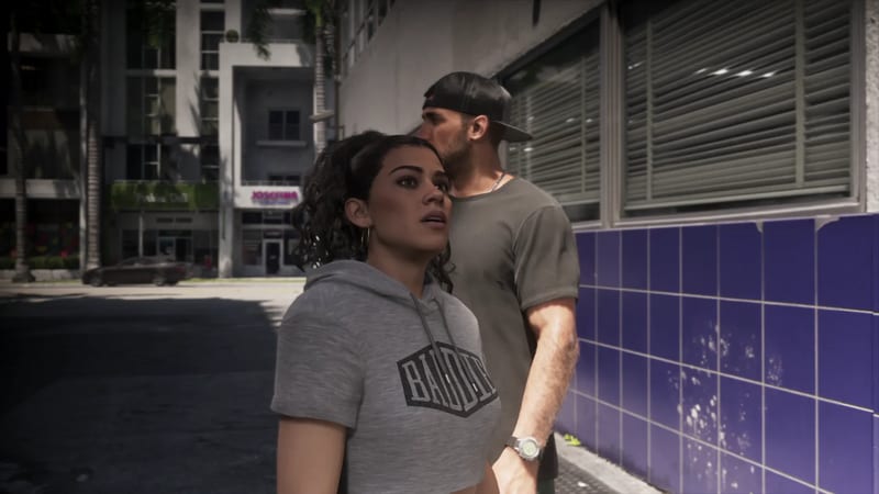 Lucia Caminos looks up beside a man in a backwards cap, next to a purple-tiled wall on a sunlit city street.