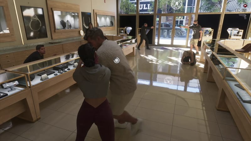 A woman in a grey cropped hoodie grapples with a man in a cream shirt inside a jewellery shop while masked robbers point guns near the glass doors.