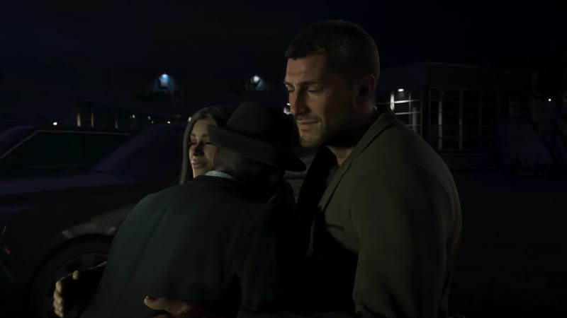 Jason Duval, in an olive jacket, embraces an older man in a brimmed hat while a smiling woman looks on, outside at night by a parked dark car.