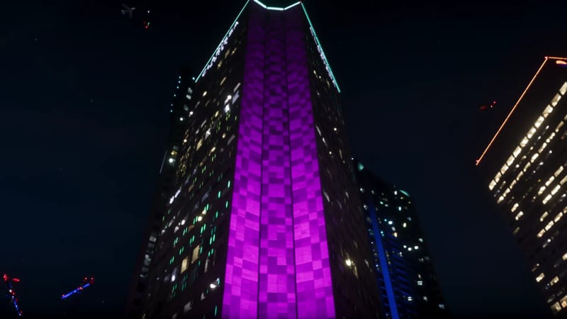 Looking up at a tall skyscraper at night, its middle glowing purple in a checked pattern, with a teal-lit crown and other lit towers beside it.