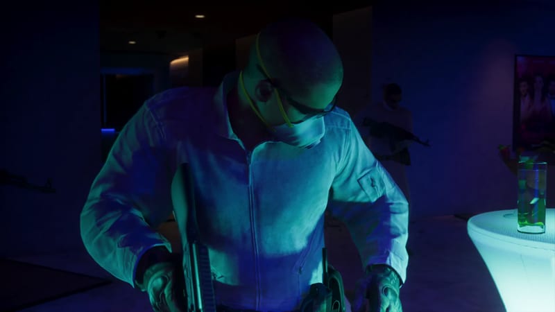 A bald man in a white boiler suit, face mask and glasses looks down, holding a rifle, in a dark room lit blue and green, with another armed figure behind him.