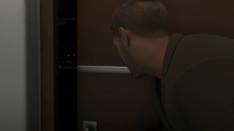 A man in a dark olive top leans towards a dark wooden door and peers through a narrow gap at distant city lights at night.
