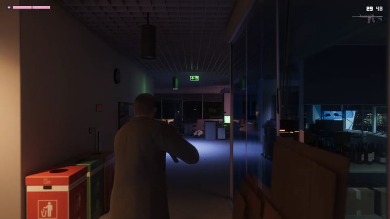 A man in a dark jacket aims a rifle along a dim office corridor lit by a green exit sign, with a body lying on the floor ahead.