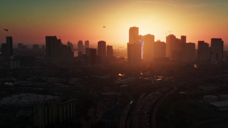 The sun sets behind the Vice City skyline, with a motorway in the foreground and helicopters flying over the silhouetted towers.