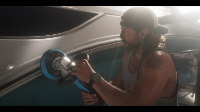 A bearded man in a backwards cap and grey vest polishes the white hull of a boat with a blue power buffer in a bright, hazy boatyard.