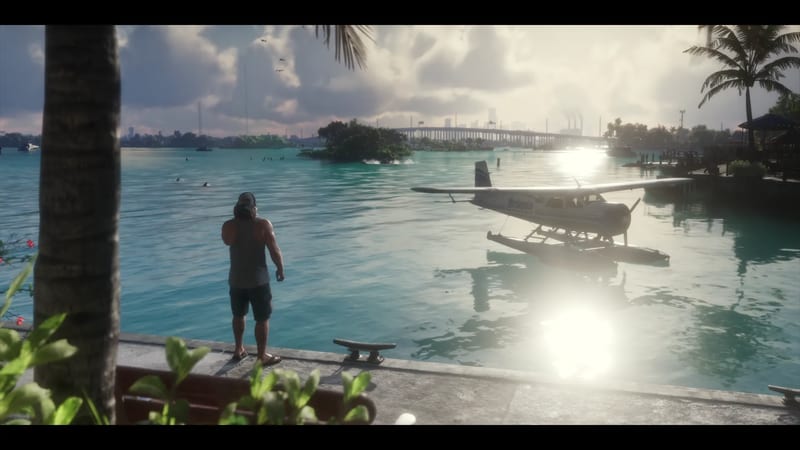 A man in a vest and cap stands on a harbour edge looking at a seaplane floating on turquoise water, with a long bridge beyond in the Leonida Keys.