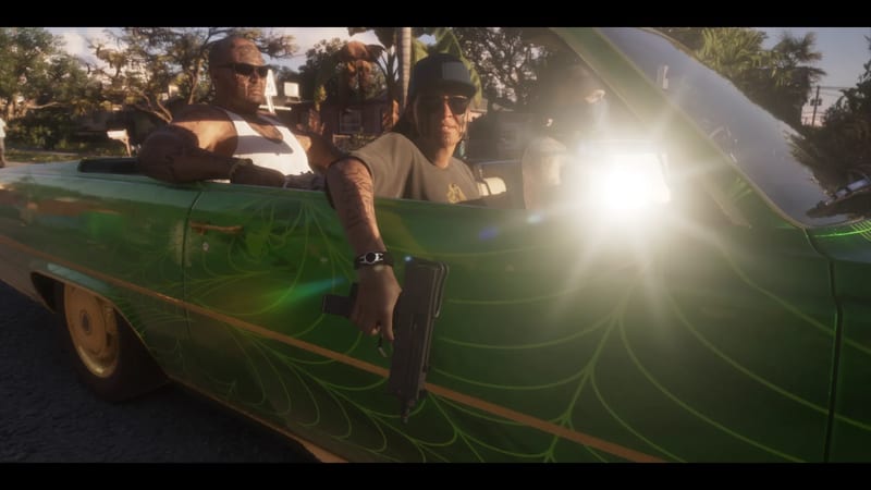 Three men ride in a green convertible with a spiderweb paint design; the front man holds a compact submachine gun out of the car on a sunlit street.
