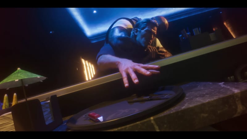 A man in a dark top lunges across a marble bar towards a tray holding a pen and a small red object, in a dimly lit club lit blue.