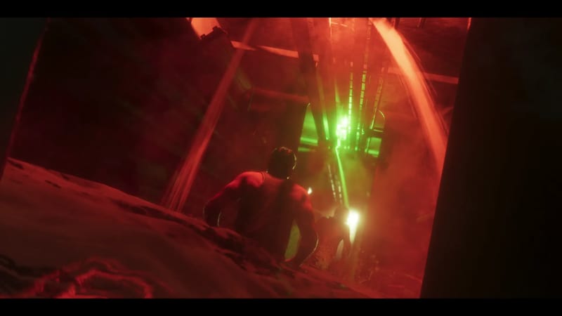 A shirtless man with dark hair seen from behind crouches on a slope, looking down a dark red-lit shaft towards a bright green light and glowing figures.