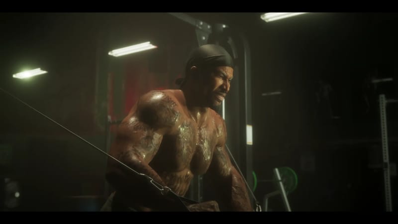 A shirtless, heavily tattooed muscular man in a dark durag grimaces as he pulls a cable handle in a dimly lit gym.