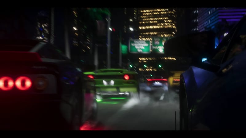Sports cars, one lime green, queue on a night-time city street lined with lit skyscrapers and green motorway signs in Vice City.