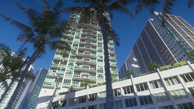 Palm trees frame a tall white apartment tower with green-tinted glass and curved balconies under a clear blue sky in Vice City.
