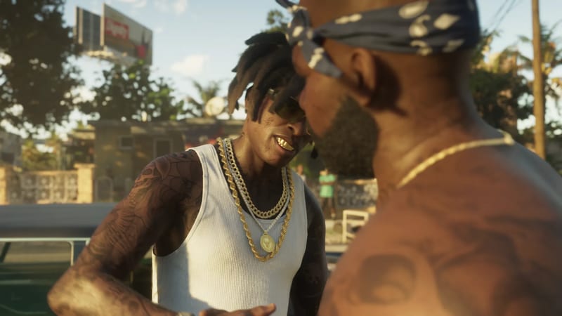 Two men talk face to face on a sunny street: one in a white vest and gold chains, the other in a dark patterned bandana, seen from the side.