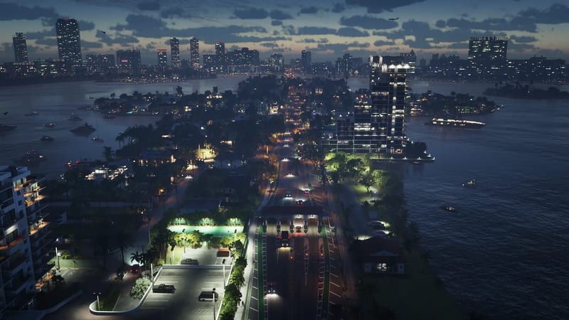 Aerial view at dusk of a causeway with a toll plaza running between waterside islands, with a lit city skyline in the distance in Vice City.