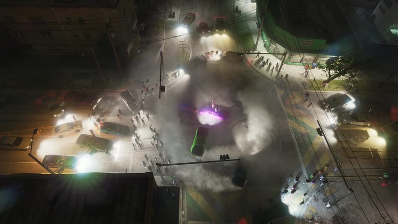 Overhead view of a night-time street takeover, with cars spinning in white tyre smoke at a crossroads while crowds watch from the roadside.