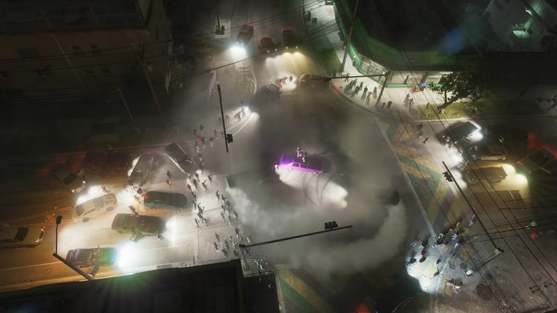 Aerial view at night of a purple car doing a burnout in a smoky street junction, surrounded by parked cars with bright headlights and a crowd of onlookers.