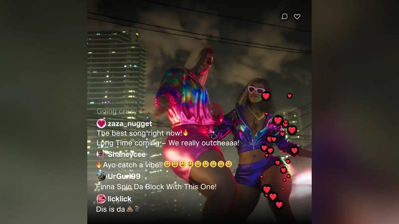Two women in shiny, colourful tracksuit jackets and shorts dance on a rooftop at night, with a city skyline behind and live-stream comments over the picture.