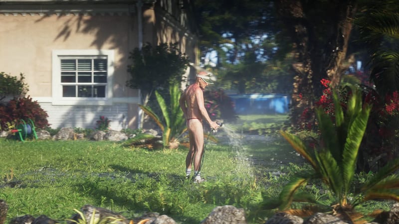 A man in a white visor, red thong and white socks waters a sunny front garden with a hose beside a peach-coloured house.