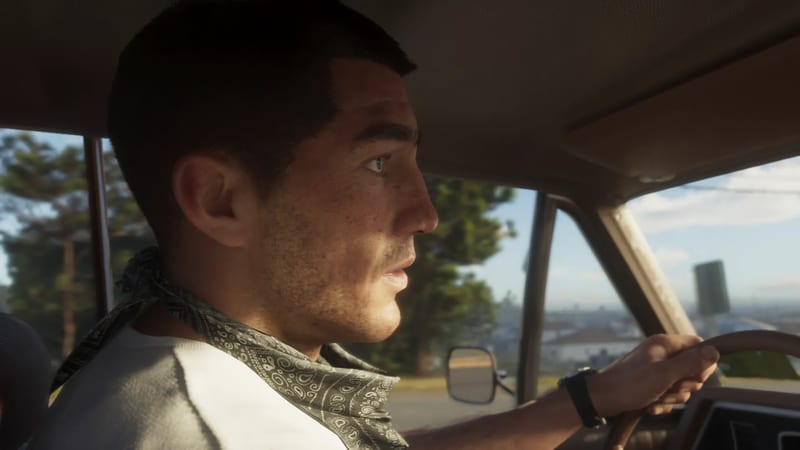 Jason Duval drives a car in profile, one hand on the steering wheel, wearing a grey paisley bandana, with a hazy city view behind him in daylight.