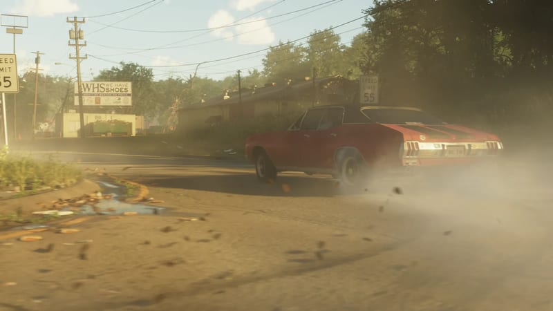 A red car with dark stripes skids round a bend on a dusty road, kicking up a cloud of dust, past speed limit signs and a shoe billboard.