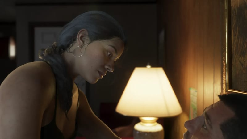 Lucia Caminos leans over a man lying in bed beside a lit lamp in a dimly lit, wood-panelled room.