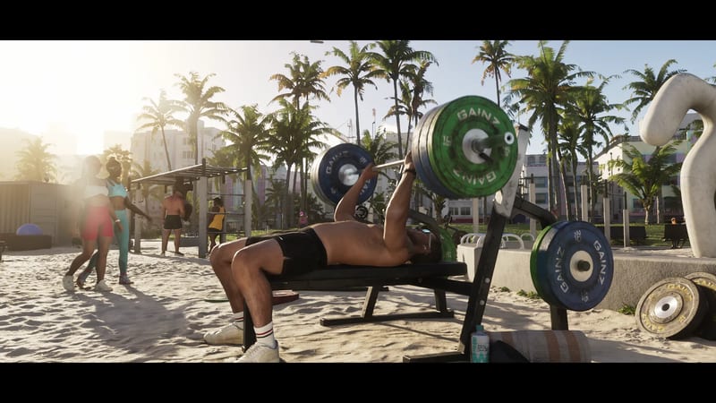 A shirtless man bench-presses a barbell with green and blue GAINZ plates on a sandy beach gym, with palm trees and pastel buildings behind.