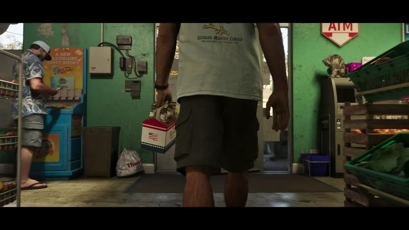 A man in a pale Leonida Marine Center T-shirt and cargo shorts walks into a green-walled shop holding a six-pack of beer, as another man looks on.