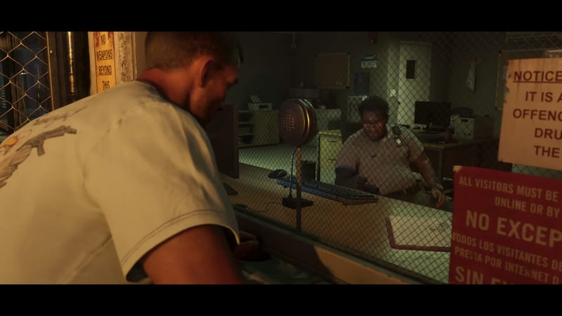 Jason Duval leans towards a glass and mesh screen to speak to a uniformed guard at a desk in Leonida Penitentiary's visitor area.
