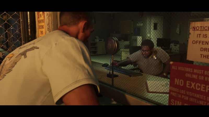 A man in a pale T-shirt leans towards a uniformed officer behind a mesh-covered window at a reception desk in a dim, greenish-lit office.