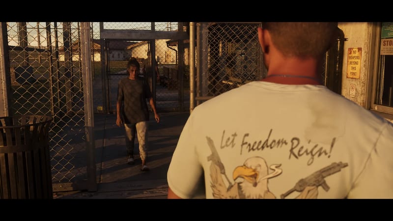 A man in a white T-shirt seen from behind watches a woman walk towards him through a chain-link gate at golden hour.