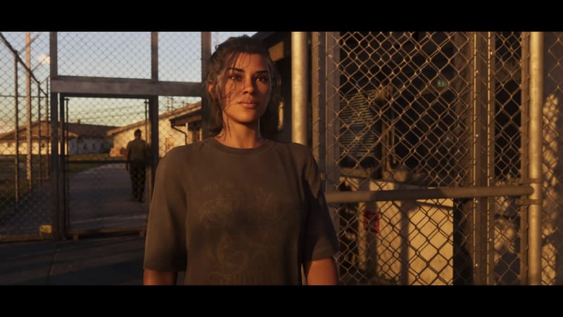 Lucia Caminos stands in a grey T-shirt beside chain-link fences at Leonida Penitentiary, lit by low golden sunlight.
