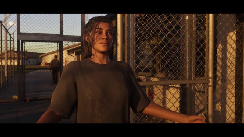 Lucia Caminos stands in warm evening light beside chain-link fencing at Leonida Penitentiary, with a guard walking away behind her.