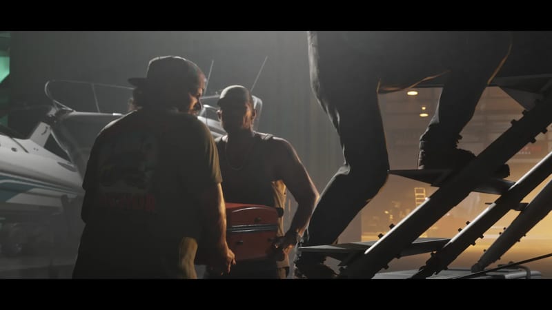 Two men in caps carry a red suitcase between them in a dim boat storage building, beside white motorboats and a set of metal steps.