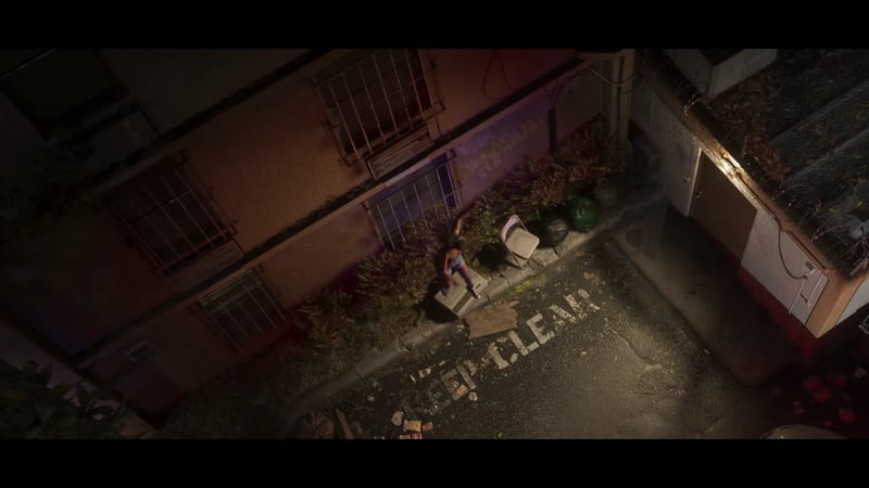 From above, a person in shorts raises one arm beside a low wall and bushes in a dim back alley at night, with 'KEEP CLEAR' painted on the road.