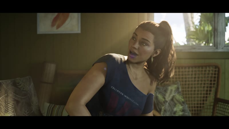 Lucia Caminos, a woman with a high ponytail and hoop earrings, turns and speaks in a sunlit room with wicker chairs and a window onto palm leaves.