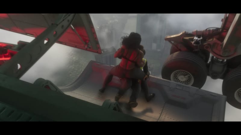 Two people embrace on an open aircraft ramp beside large landing gear wheels, high above a hazy city skyline.