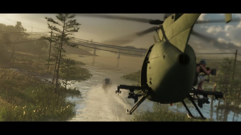 A green helicopter with a camera operator on its skid chases an Airgator Airboat 09 along a flooded road through marshland at golden hour.